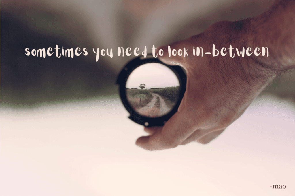 hand holding circle lens with a blurred background and clear image in lens.
depicting time flies by us so we sometimes don't notice how far we have come until we reflect.
poem title "sometimes you need to look in-between" written over image.