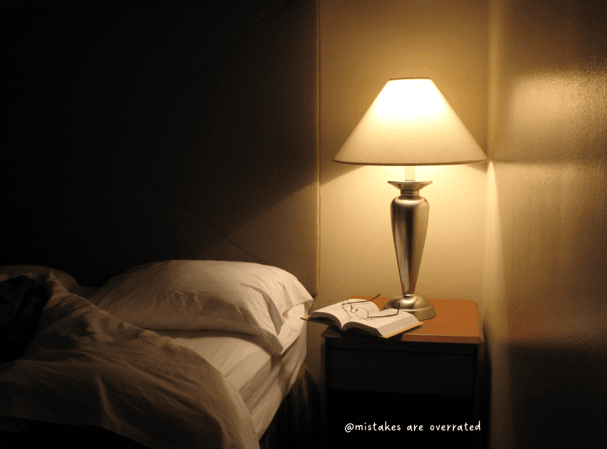 bedside table light on with book open next to bed